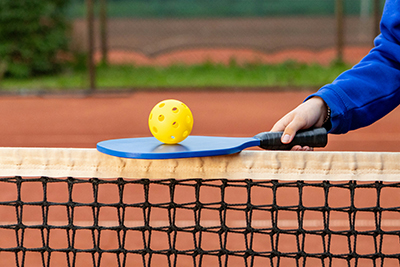 pickleball paddle held atop a net, balancing a yellow ball